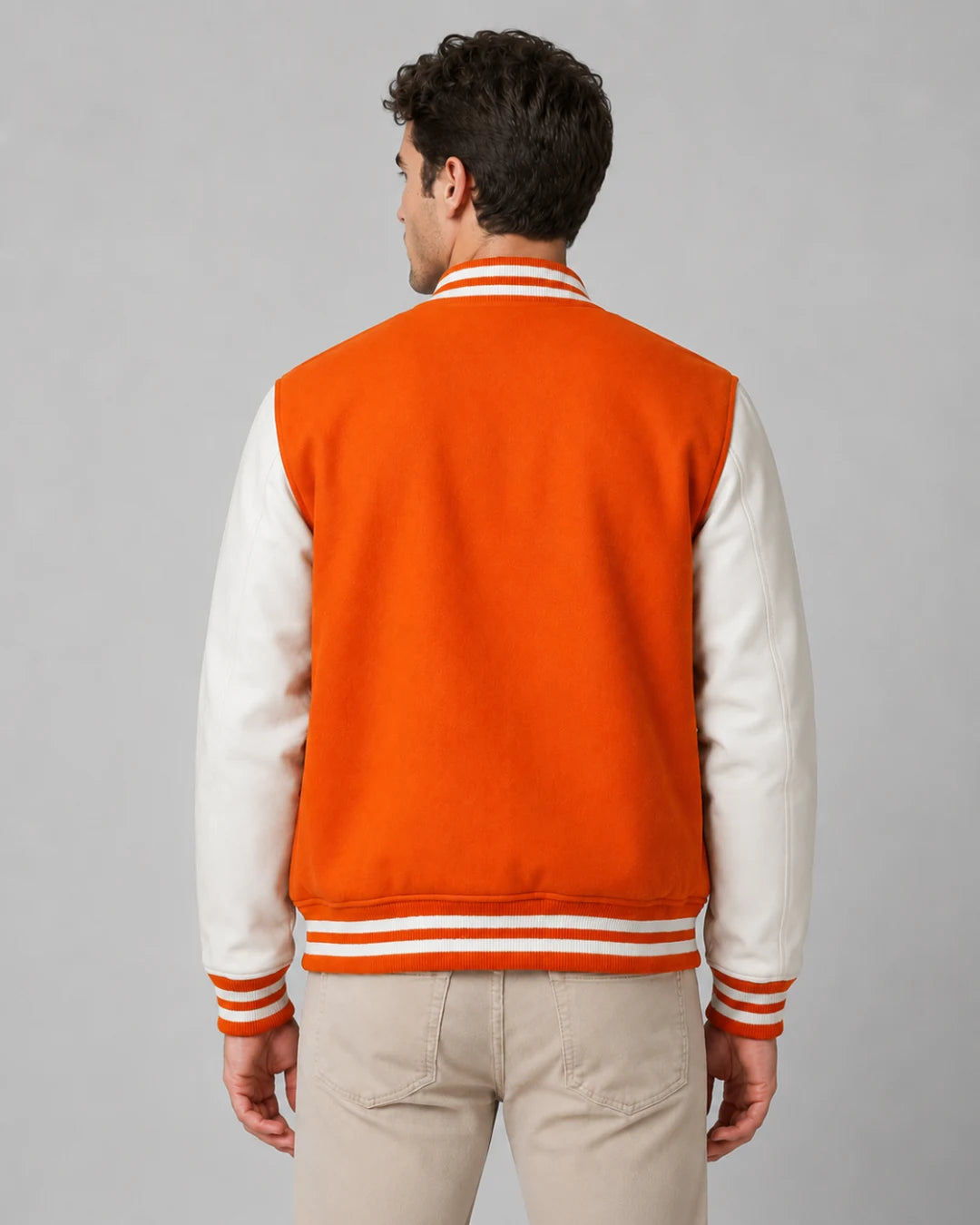 Back view of mens orange varsity jacket with blank orange wool body, white leather sleeves, and striped ribbed hem on male model