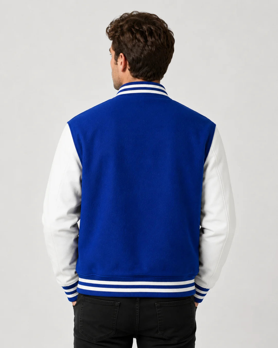 Back view of mens blue varsity jacket with blank wool body, white leather sleeves, and striped ribbed hem on male model