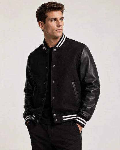 Mens black varsity jacket with wool body, leather sleeves, snap buttons, and striped ribbed trim worn by male model