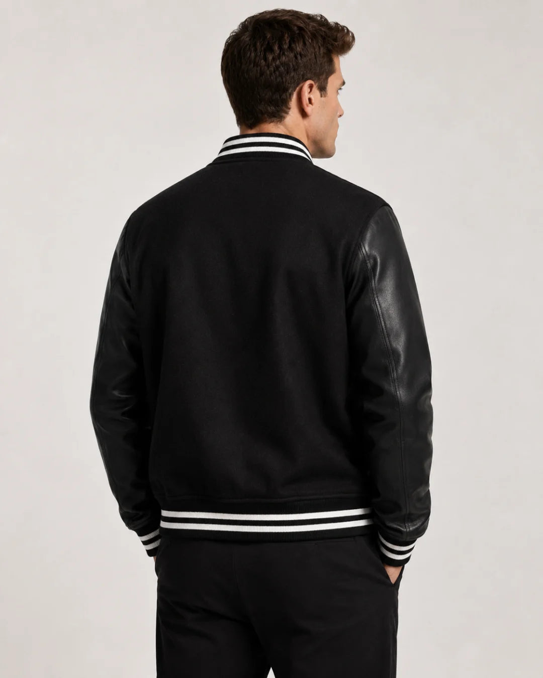 Back view of mens black varsity jacket with blank wool body, black leather sleeves, and striped ribbed hem on male model