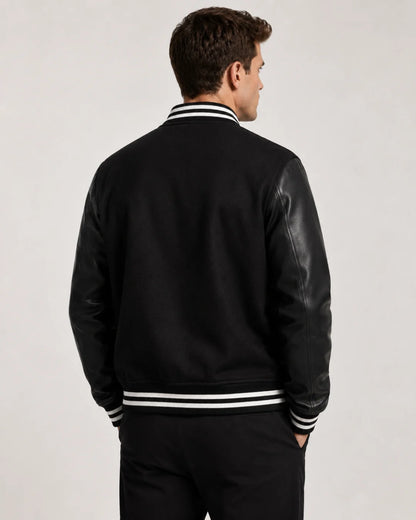 Back view of mens black varsity jacket with blank wool body, black leather sleeves, and striped ribbed hem on male model