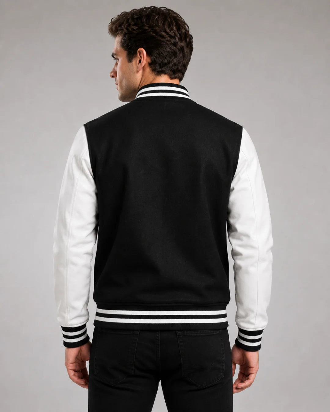 Back view of mens black and white varsity jacket with blank black wool body, white leather sleeves, and striped ribbed hem on male model