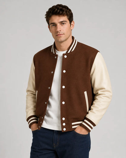 Mens brown varsity jacket with wool body, cream leather sleeves, snap buttons, and striped ribbed trim worn by male model
