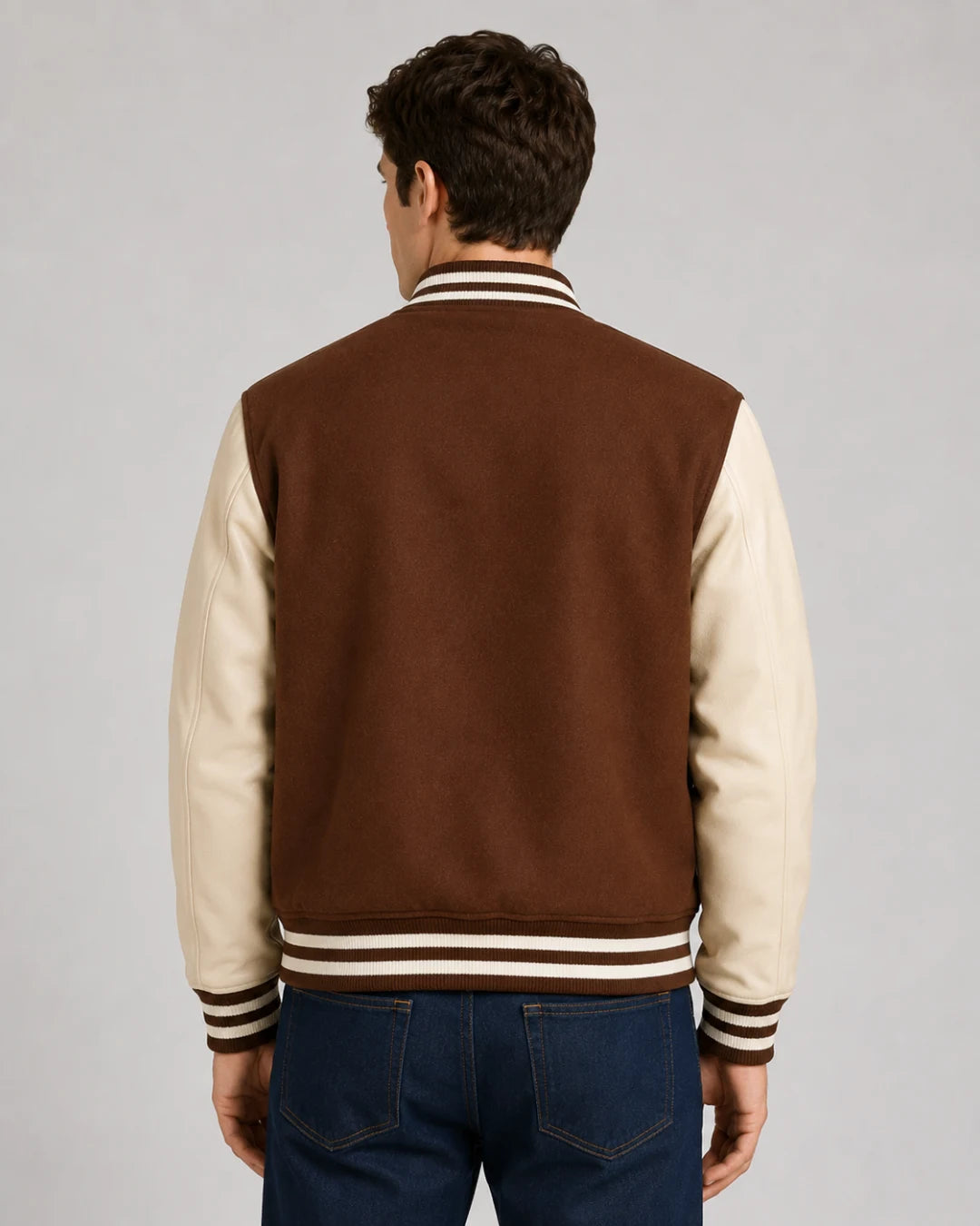 Back view of mens brown varsity jacket with blank brown wool body, cream leather sleeves, and striped ribbed hem on male model