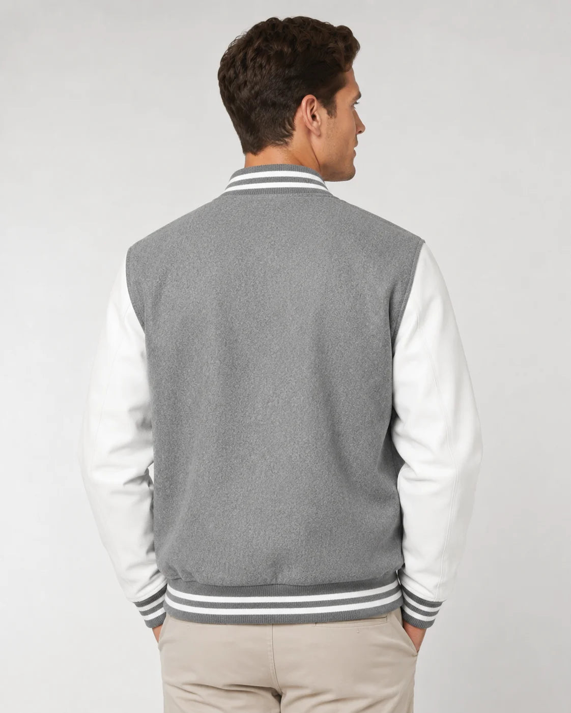 Back view of mens grey varsity jacket with blank grey wool body, white leather sleeves, and striped ribbed hem on male model