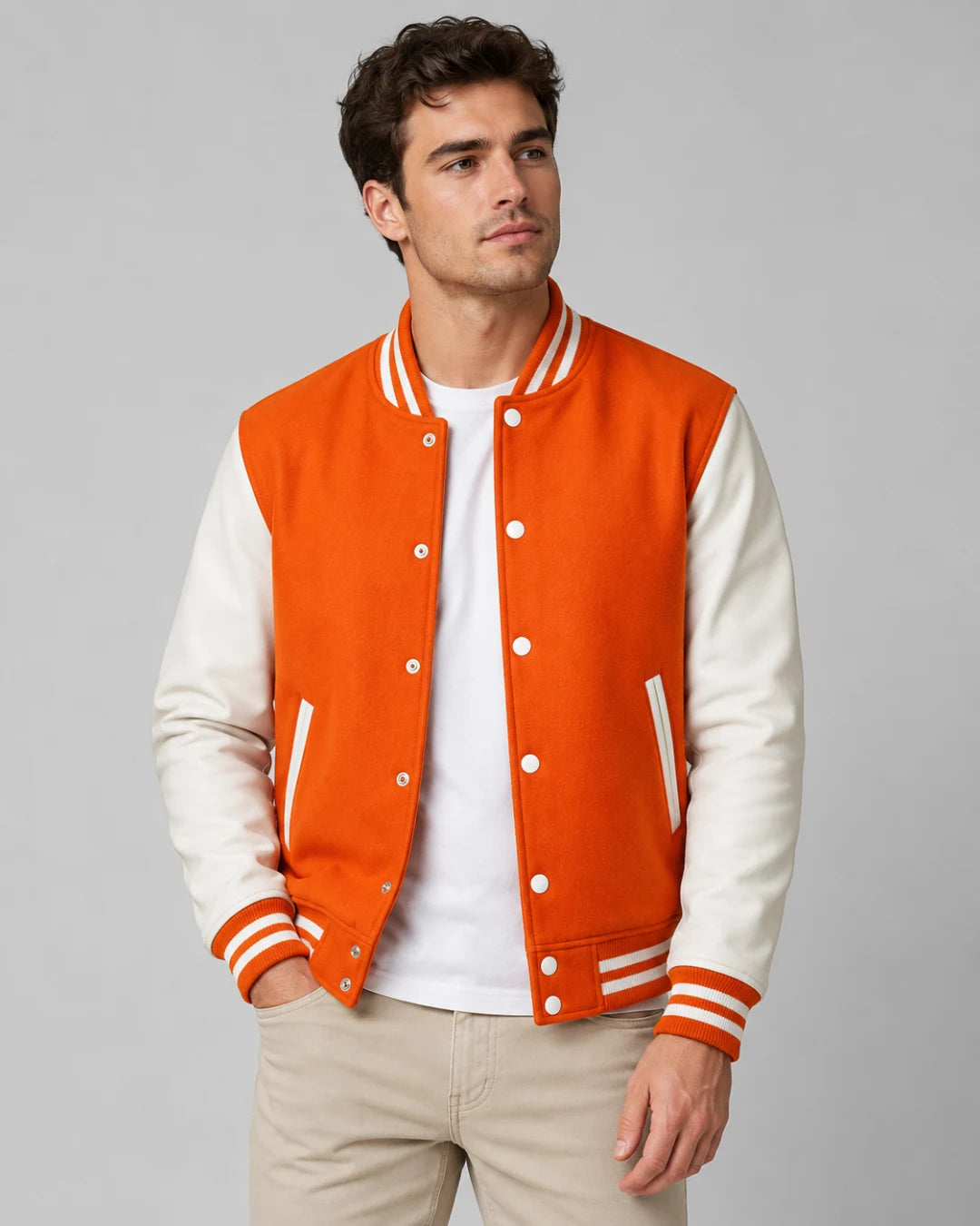 Mens orange varsity jacket with wool body, white leather sleeves, snap buttons, and striped ribbed trim worn by male model