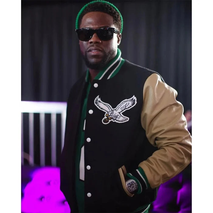 Person wearing a black and beige varsity jacket with an eagle logo, sunglasses, and a green beanie.